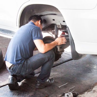 Mechanic inspecting the suspension and brakes of car at workshop.